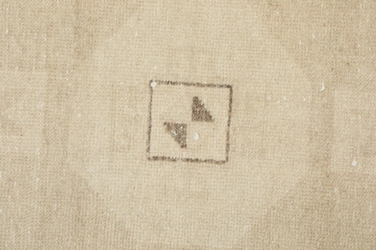 Macro shot of the low wool pile texture and faded beige color of the hand-knotted rug