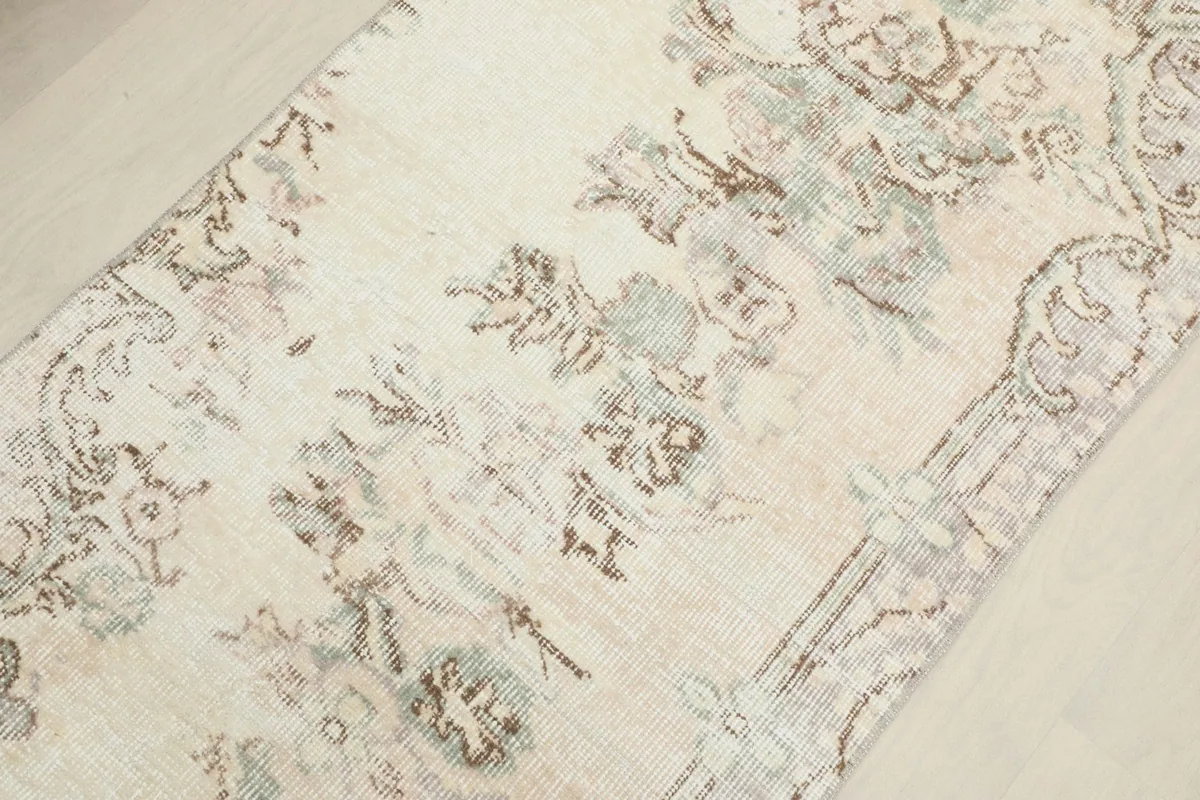 Close-up of the faded floral design and texture of the hand-knotted wool pile on the ivory runner.