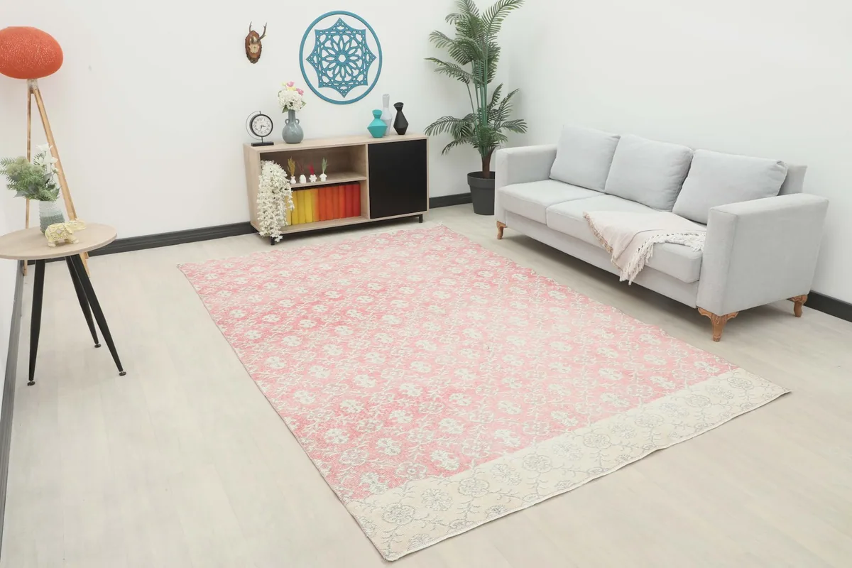 Pink and cream vintage rug displayed in a modern living room setting with a light gray sofa and wooden furniture.