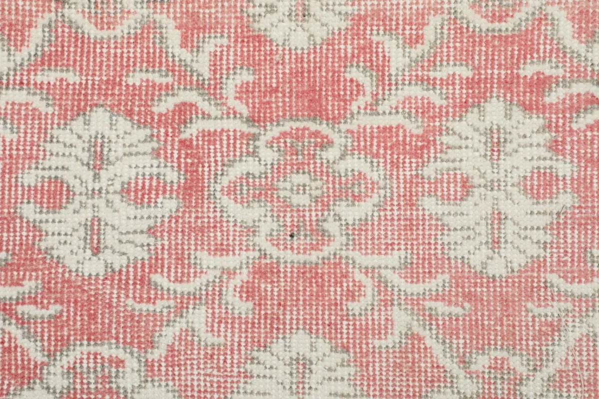 Detailed close-up of the hand-knotted wool pile, showing the texture and color variations of the pink and cream pattern.