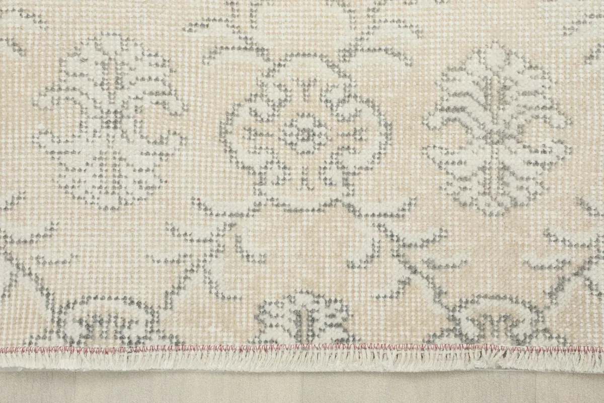 Close-up of the rug's cream border, detailing the intricate floral patterns and the subtle wear of the vintage piece.