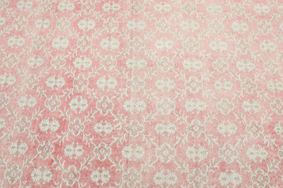 Close overhead view of the pink rug's field, showcasing the repeating cream floral and geometric motifs.