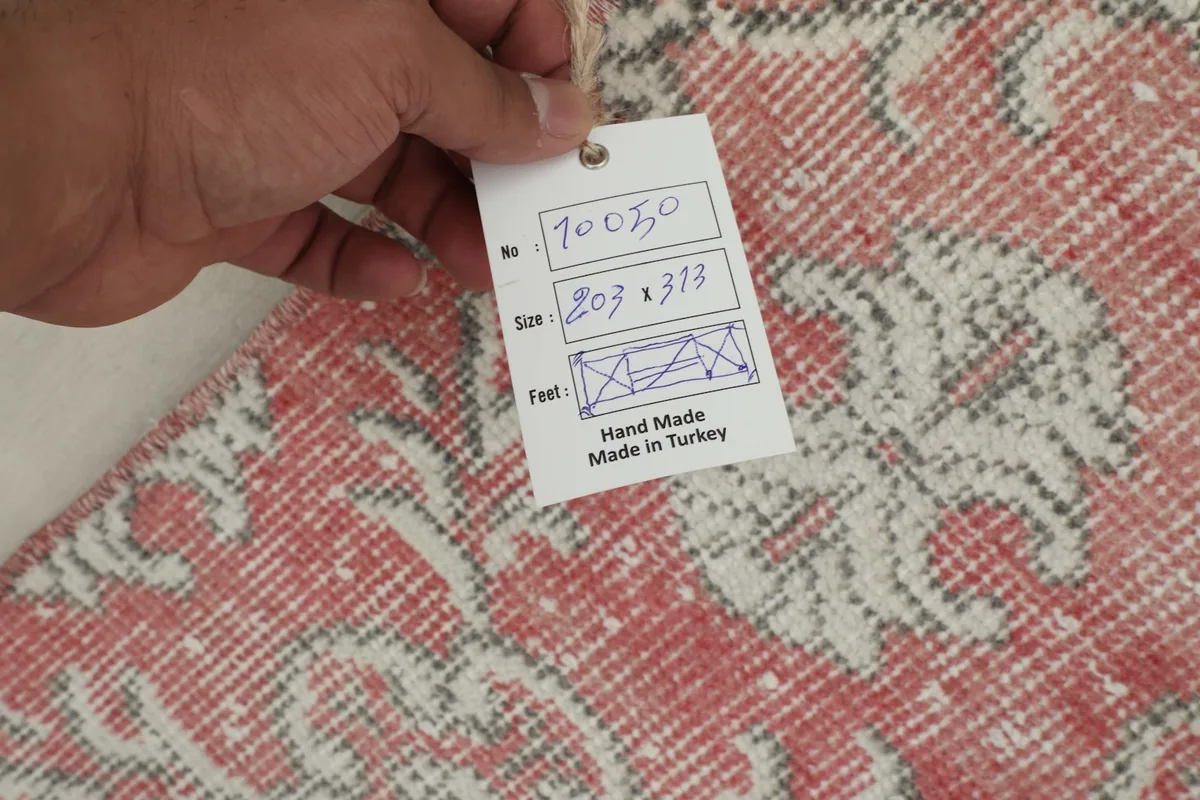Hand holding a tag displaying the rug's dimensions (203 x 313 cm) and origin, 'Hand Made in Turkey'.