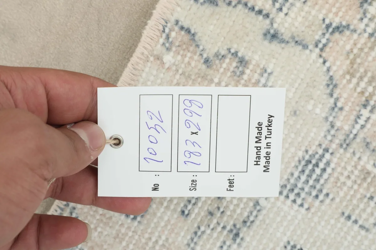 Hand holding a tag showing the rug's inventory number and 'Hand Made in Turkey'