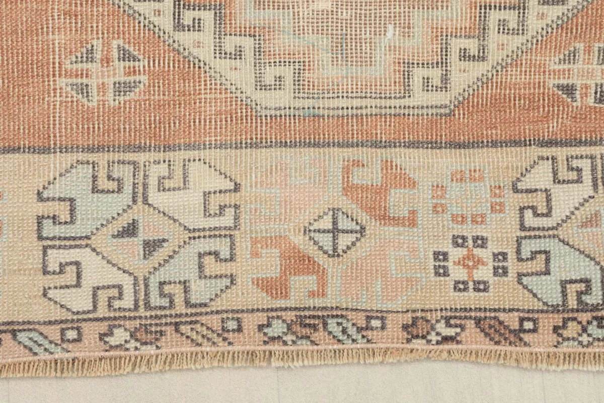 Close-up of the beige border with small geometric and tribal symbols, showing fringe