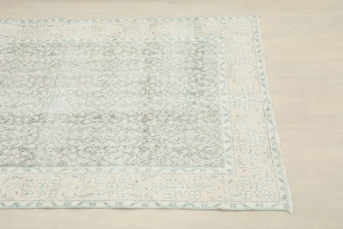 Close-up of the corner of the gray and cream rug, highlighting the faded floral patterns and border.