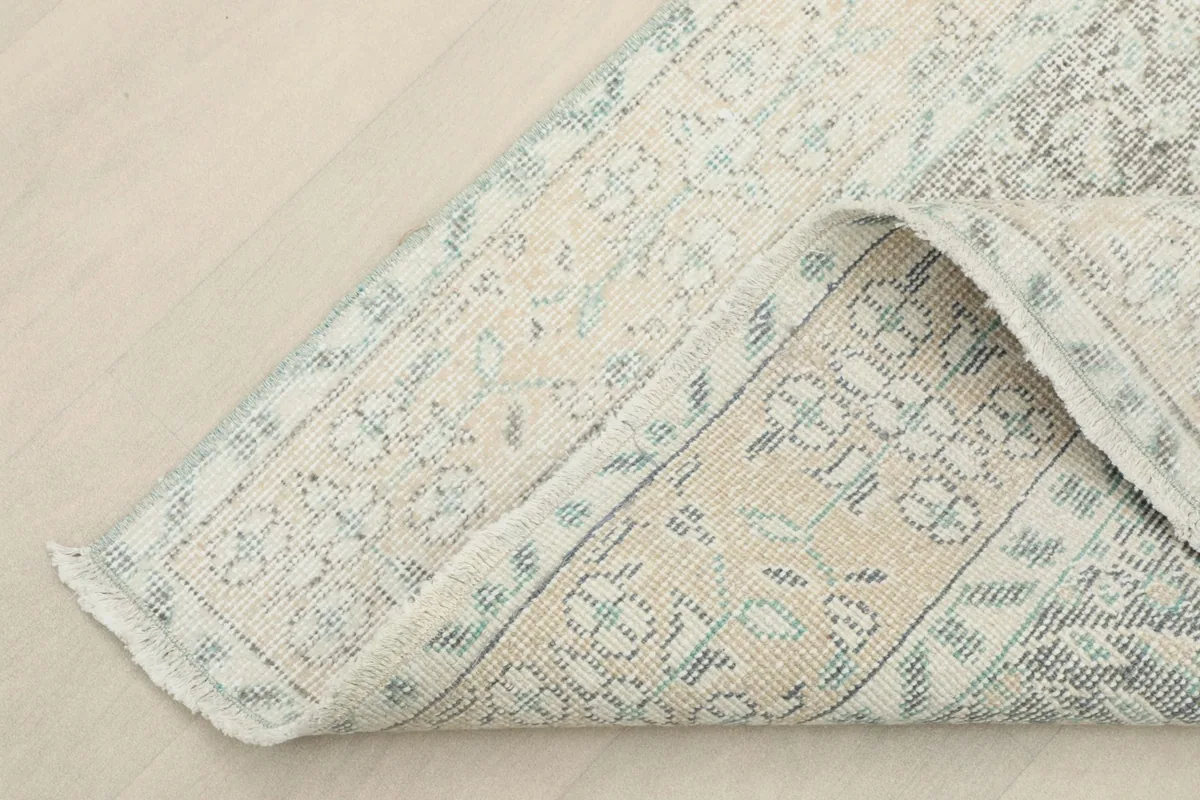View of the rug's backside and folded edge, revealing the cotton foundation and knotting.