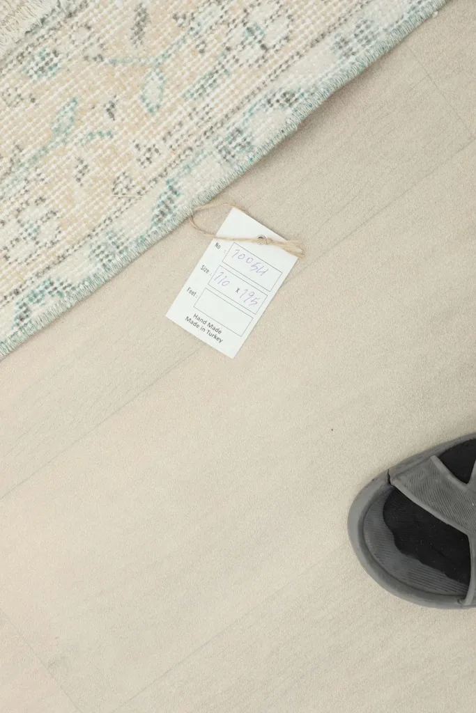 Overhead view of the rug's edge, alongside a product tag and a pair of gray sandals for scale.