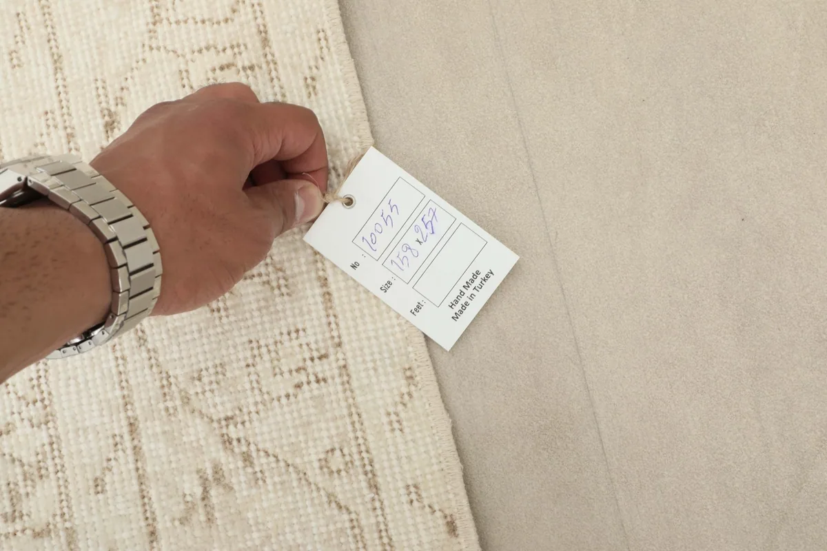 Hand holding a tag showing the rug's details, including its origin and hand-knotted construction.