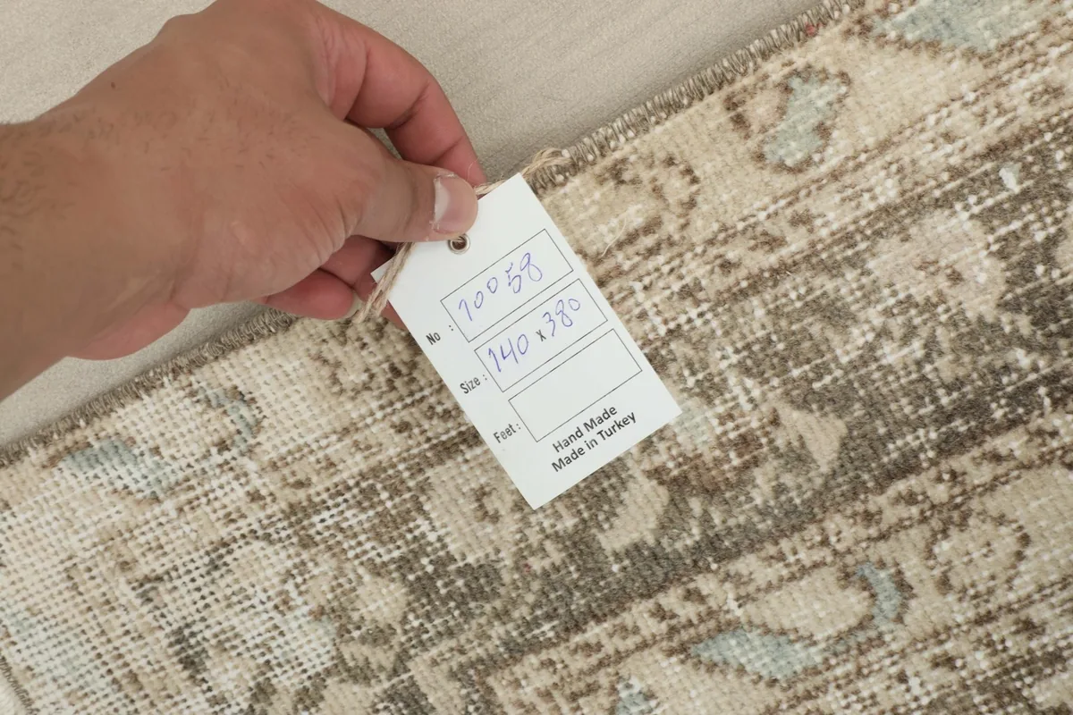 Hand holding a tag showing the rug's dimensions and 'Hand Made in Turkey'.