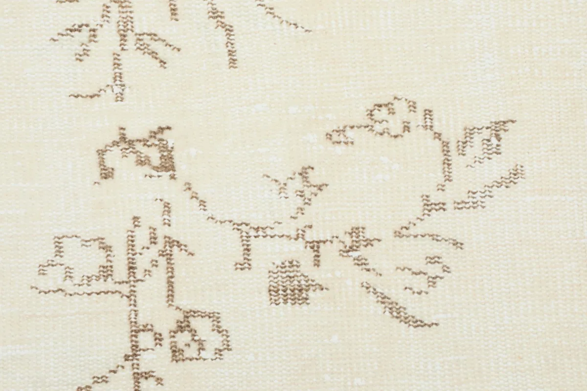 Detailed close-up of the hand-knotted beige floral pattern and ivory wool pile