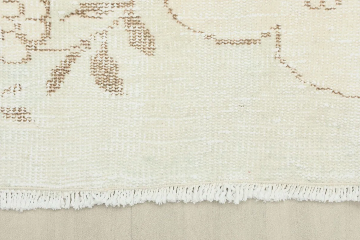 Close-up of the short, delicate fringe and edge of the vintage ivory rug