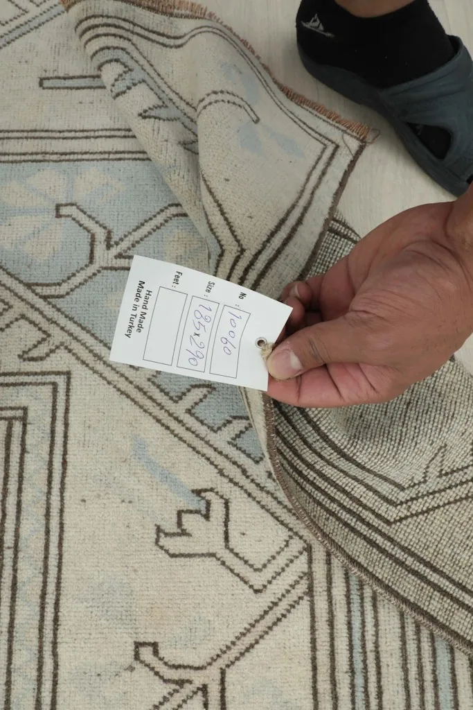 Hand holding a product tag with size and origin details over the rug