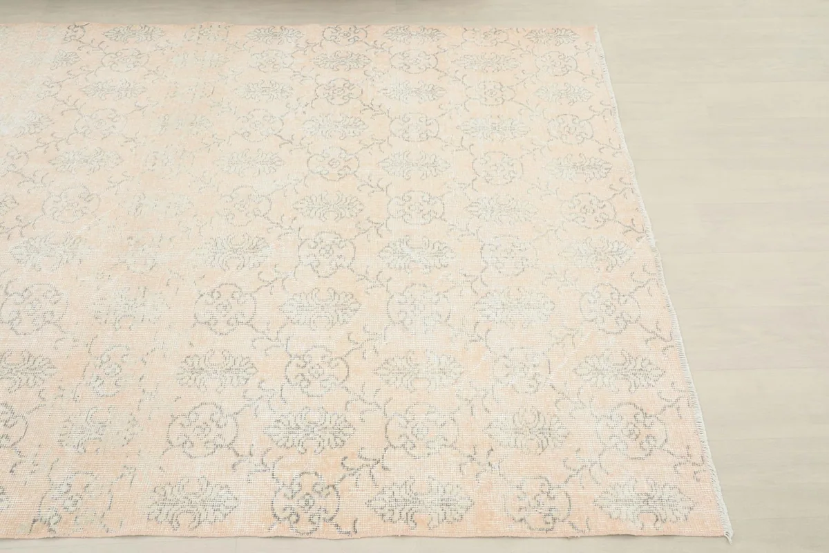 Close-up angled shot of the vintage rug, showing the faded gray floral motifs on the cream field.