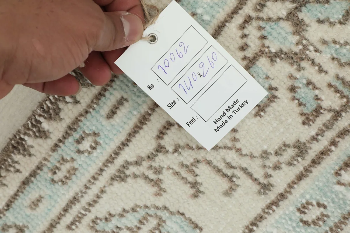 Hand holding a tag showing the rug's item number and dimensions over the pile