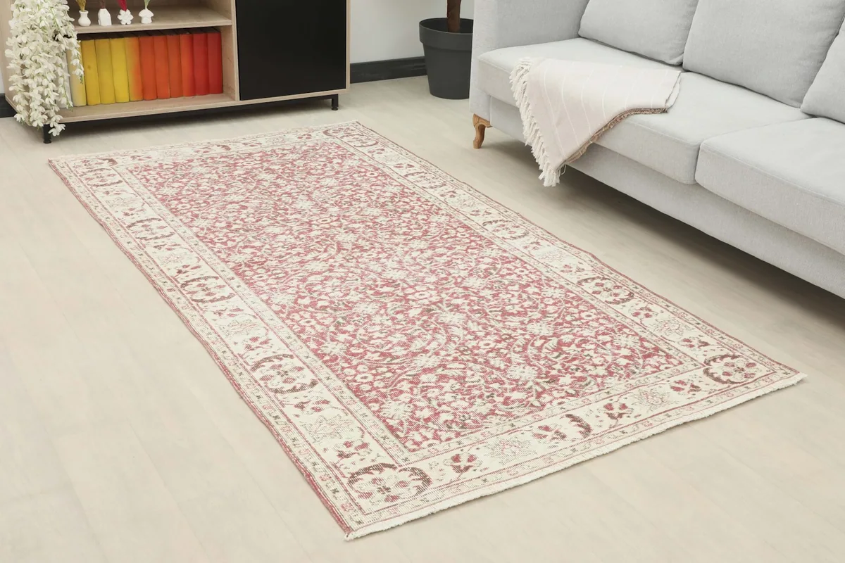 Angle view of the rose and ivory rug in a living room, showing its placement by a sofa and cabinet