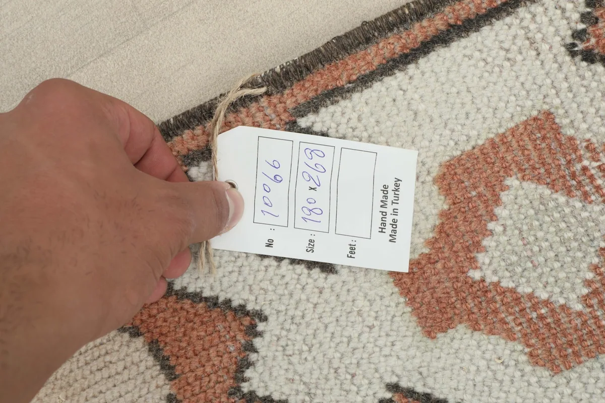Hand holding a tag showing the rug's size in cm and 'Hand Made in Turkey'