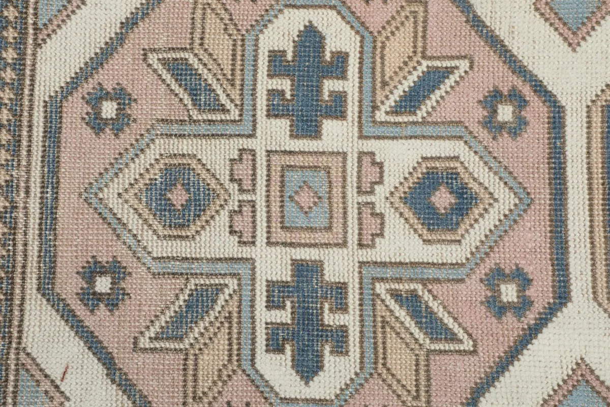 Detailed view of a rose colored geometric medallion with intricate blue and cream elements