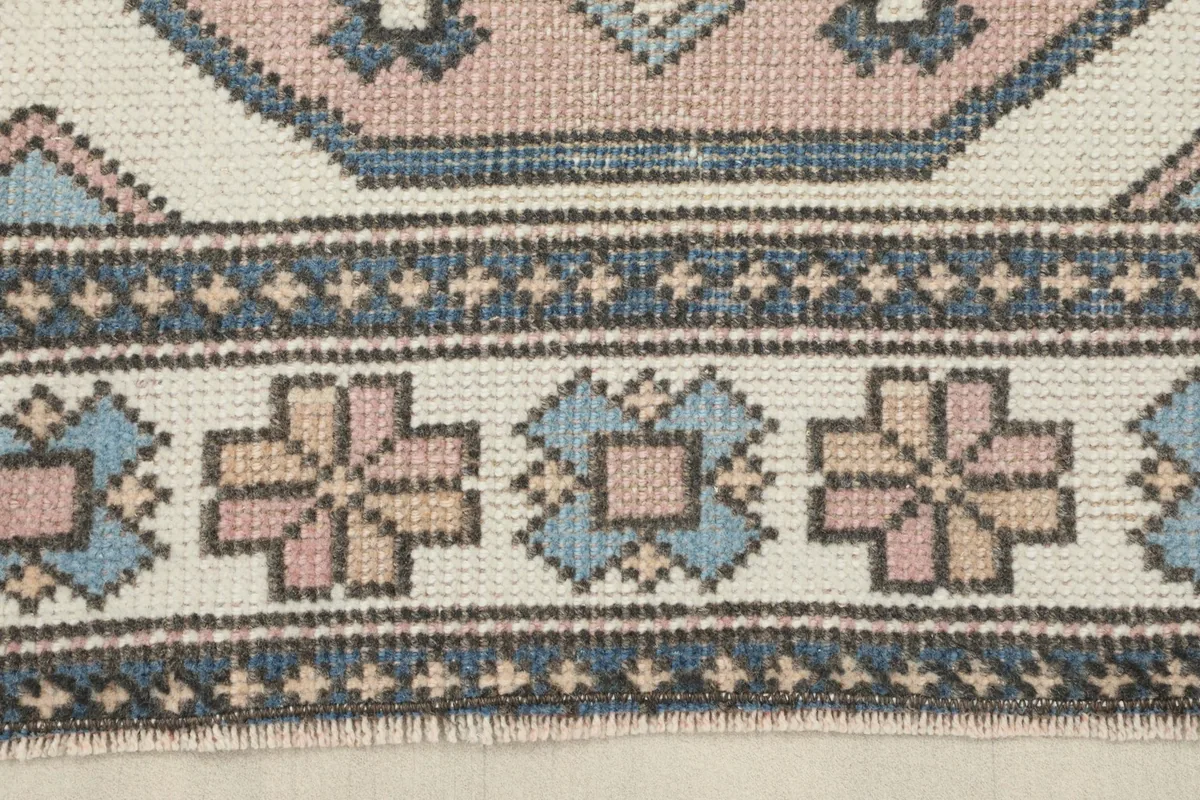 Close-up of the rug's border, displaying the repeating tribal motifs in blue, rose, and gray