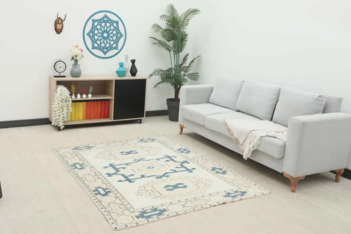 Ivory and blue geometric rug placed in a living room setting with a light gray sofa and wooden cabinet.