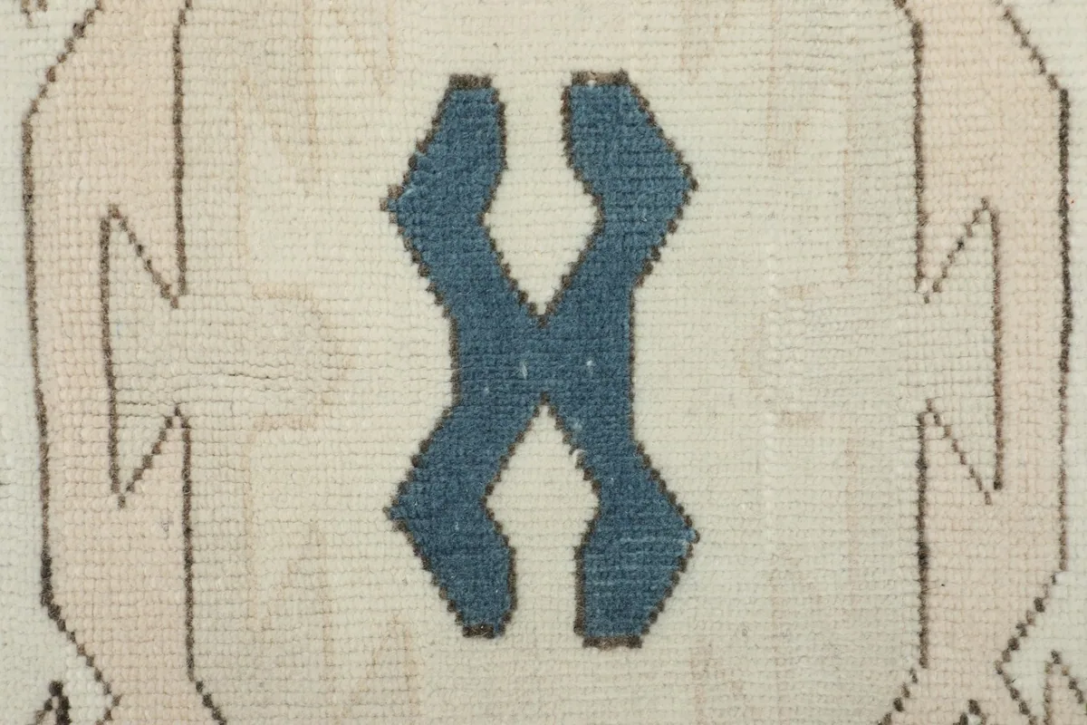 Close-up of a blue tribal motif within a tan geometric shape, showing the texture of the wool pile.