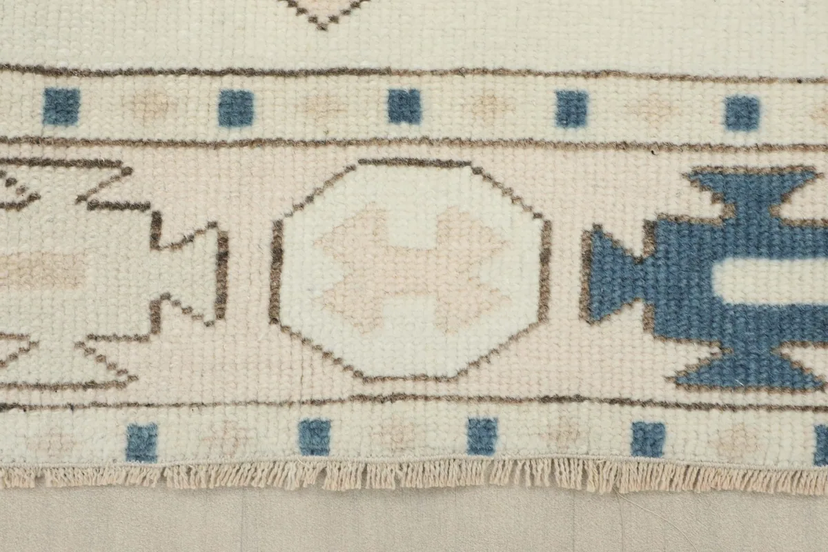 Detailed view of the rug's border, featuring blue squares and tan octagonal shapes with small fringes.