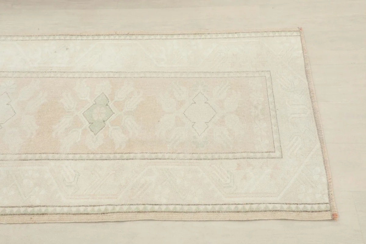 Close-up of the rug's end, showing the subtle cream, rose, and olive geometric patterns and border.