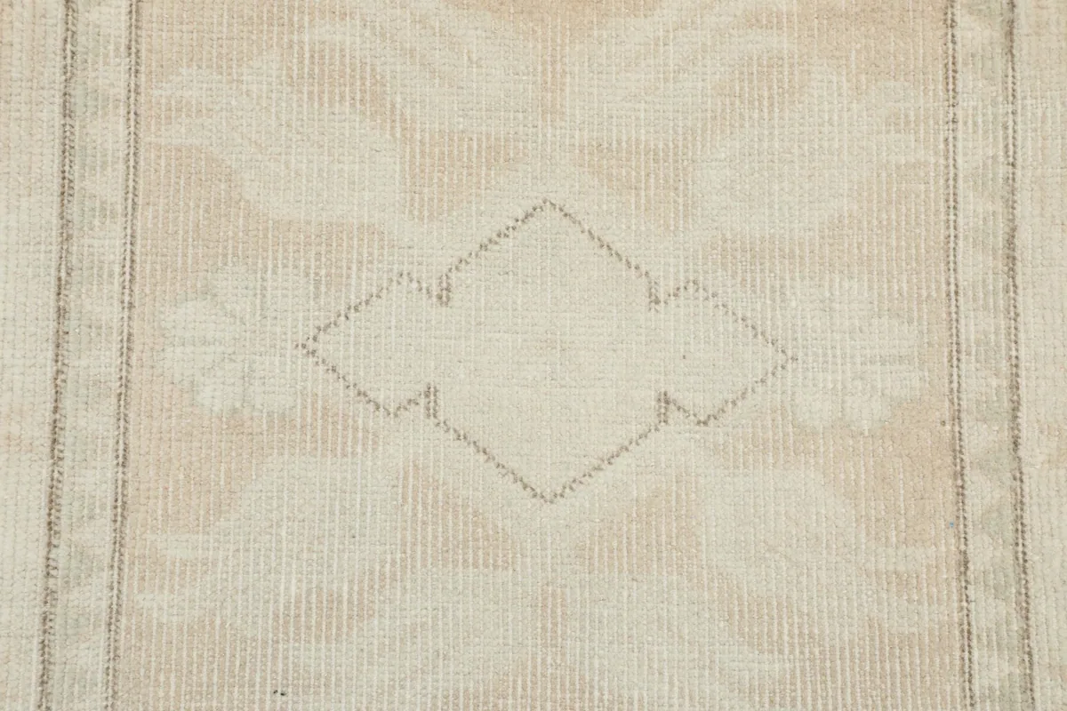 Close-up of a central geometric diamond motif in olive and cream, illustrating the hand-knotted detail.