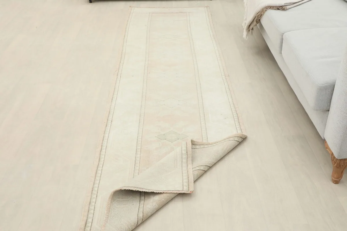 The cream runner rug partially folded in a room setting, demonstrating its flexibility and construction.
