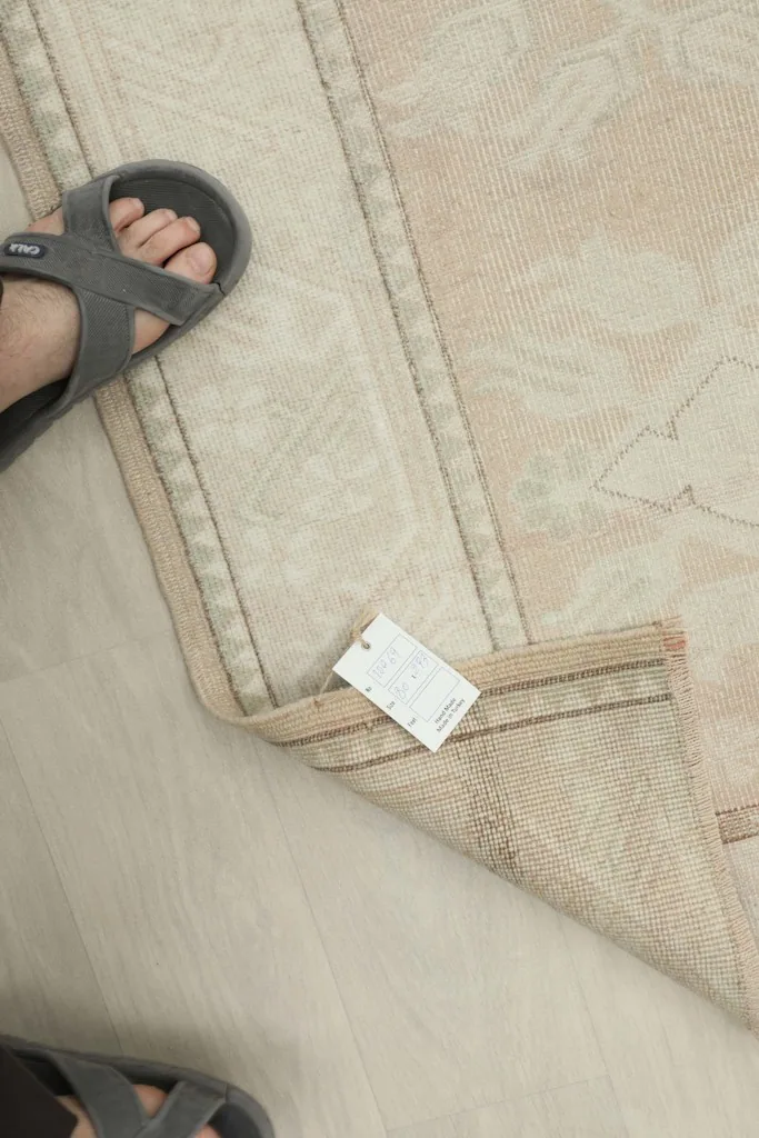 Close-up of the rug with a foot and a tag, showing scale and texture of the low pile.