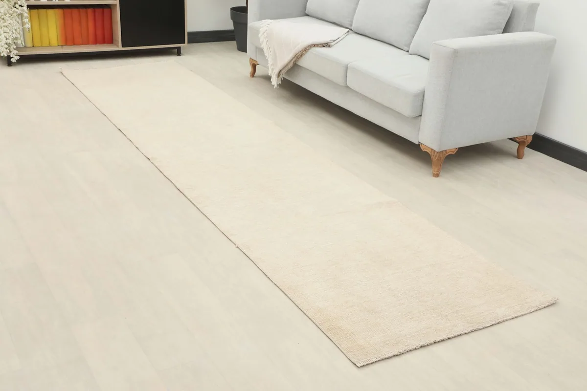 Angled view of the cream runner in a room, highlighting its length and neutral tone beside a sofa