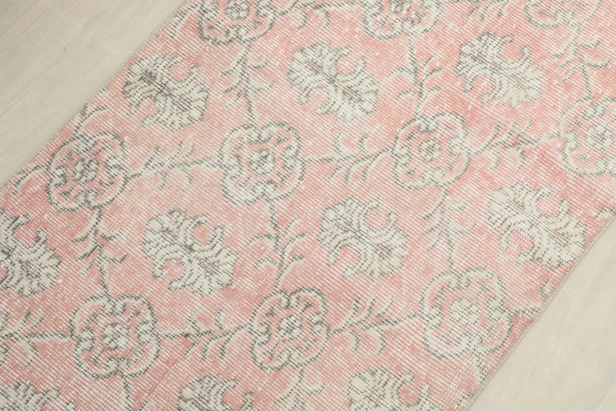 Diagonal view across the pink rug, highlighting the repeating floral patterns.