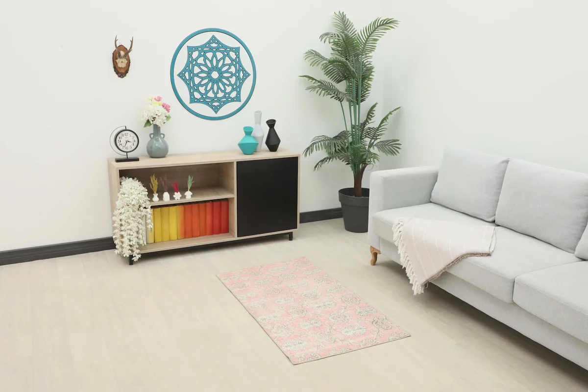 Pink floral vintage rug displayed in a living room setting with a light gray sofa and wooden cabinet.
