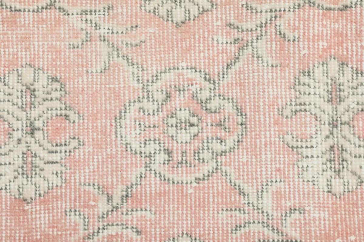 Detailed close-up of a central gray and ivory floral motif on the pink field of the rug.