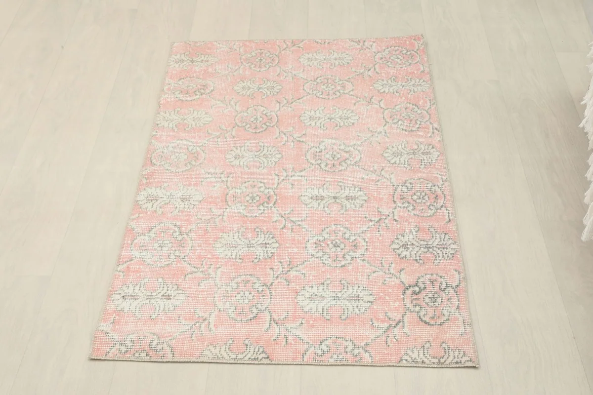 Full overhead view of the pink floral vintage rug on a light wooden floor.