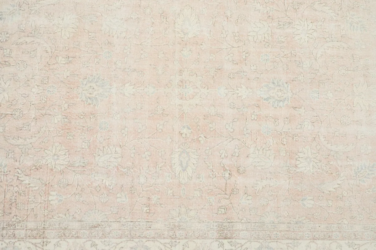 Overhead close-up showing the central field of the rug with faded floral patterns in rose, beige, and light blue.