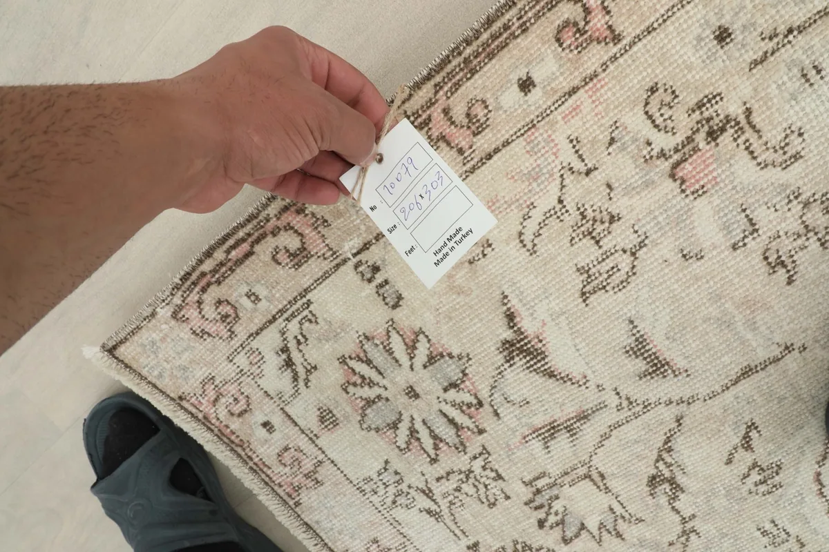 Hand holding a tag, showing the reverse side and knotting of the vintage rug