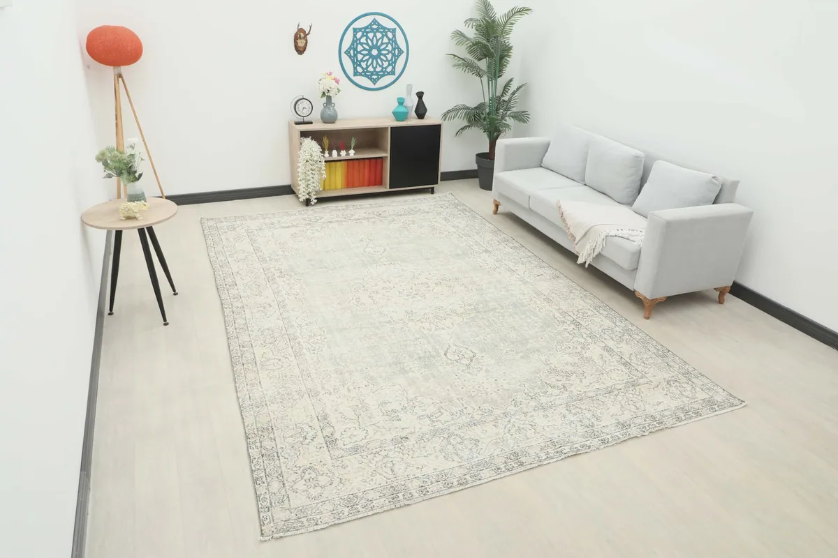 Large cream and gray vintage rug shown in a modern living room setting with a sofa and side table.