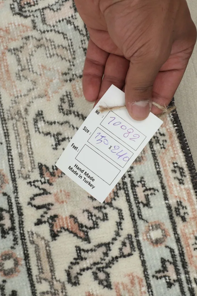Hand holding a tag showing the rug's item number and size, highlighting the handmade quality