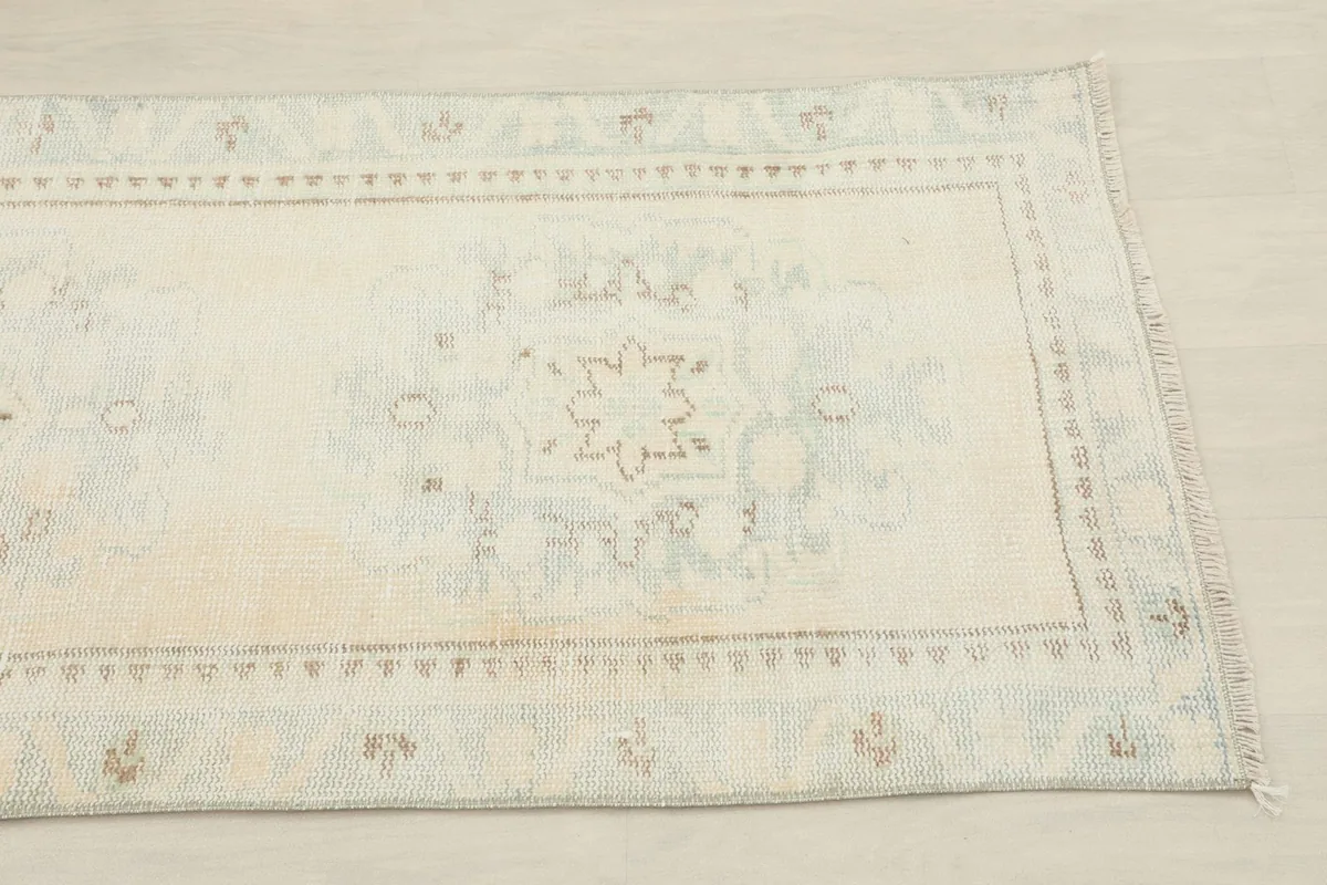 Close-up view of the rug's surface, showing subtle blue and rust geometric patterns on the cream field.
