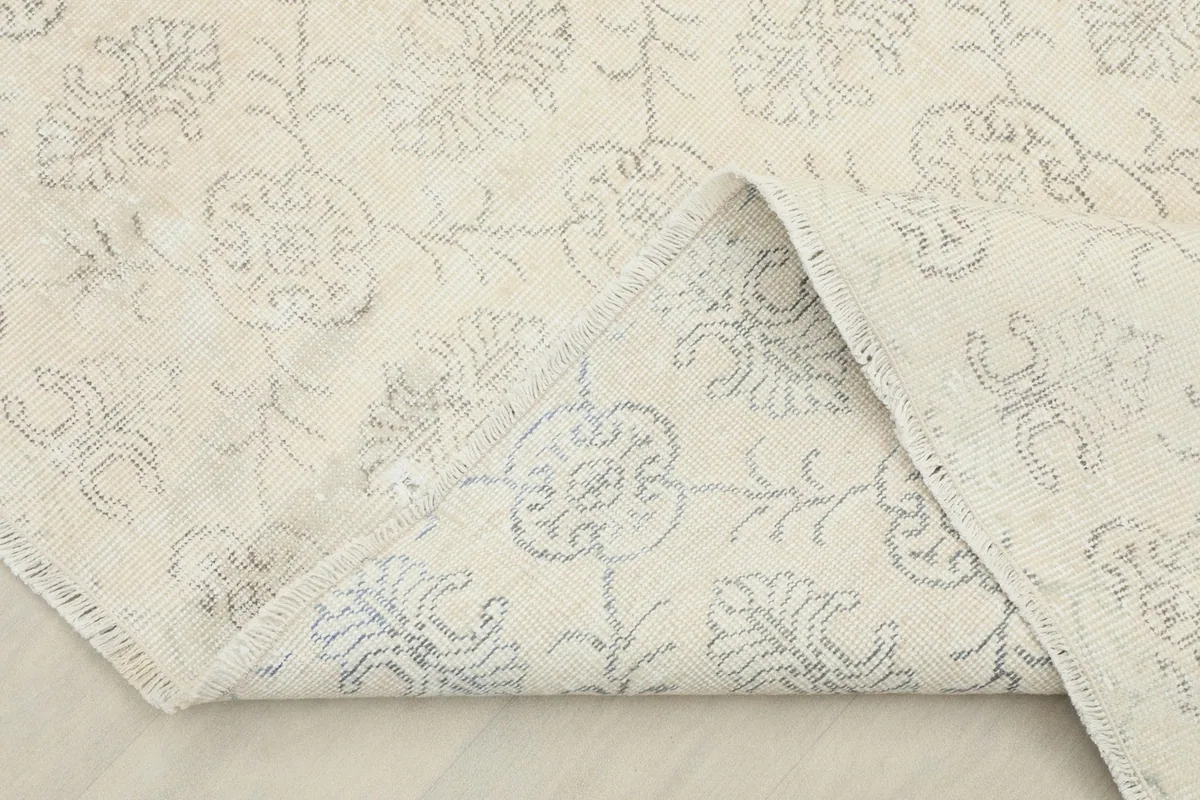 Corner of the rug folded back, revealing the cotton foundation and reverse side of the pattern