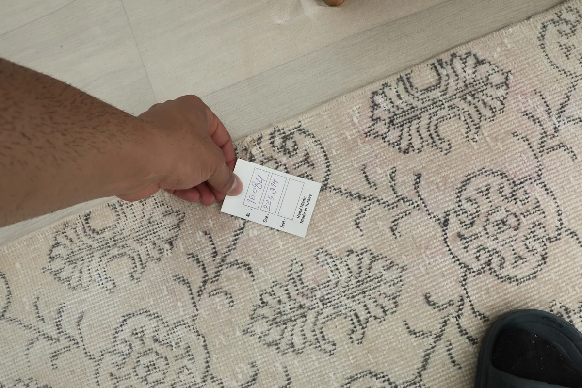 Hand holding a size tag near the rug's edge, showing the texture and pattern details