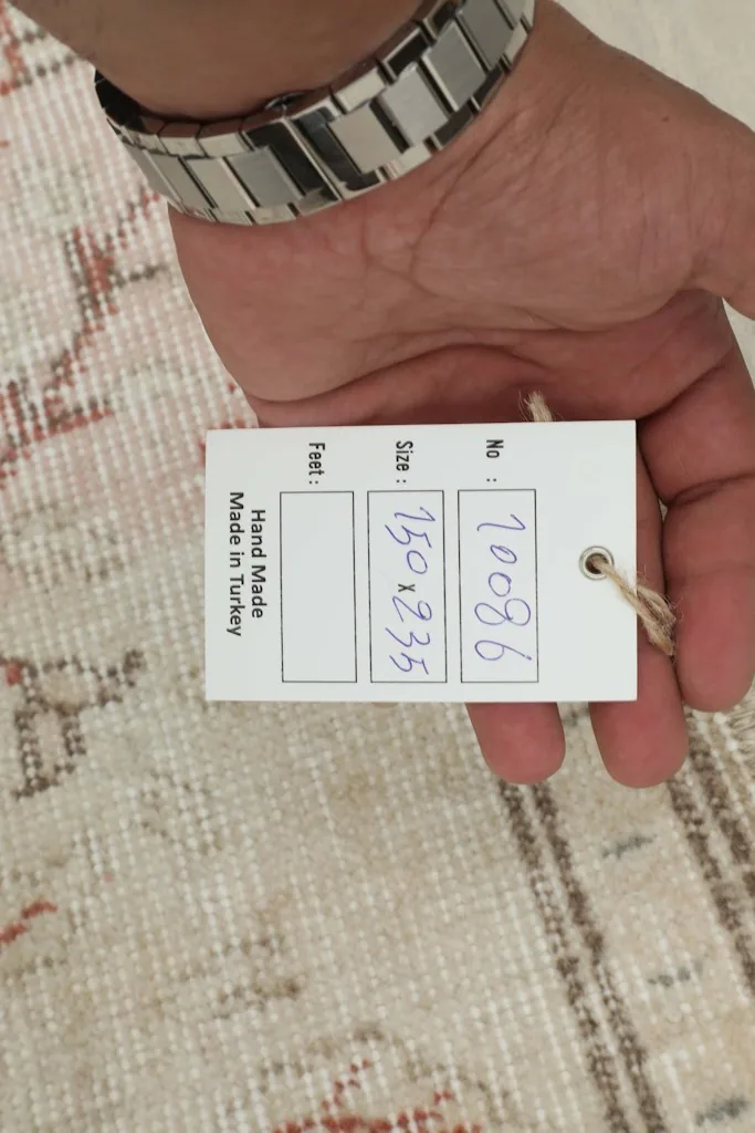 Hand holding a tag showing the rug's dimensions and origin