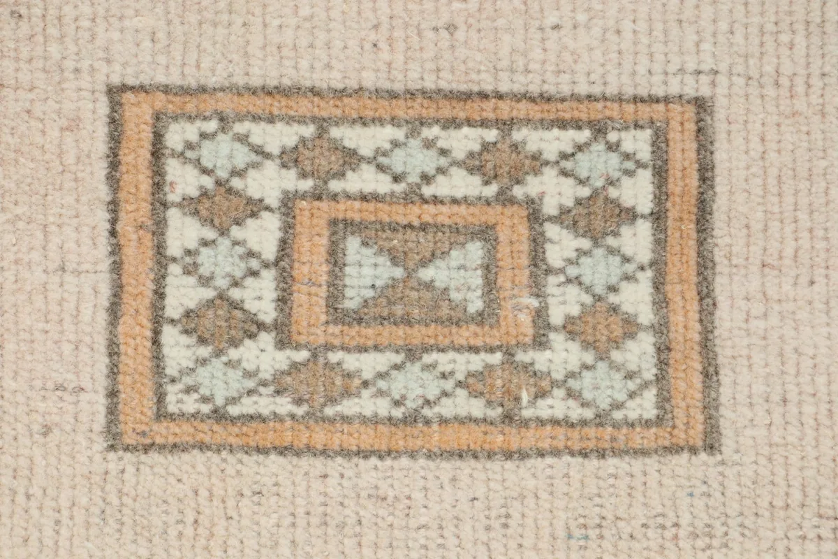 Close-up of a small square geometric motif in orange, beige, and gray tones.