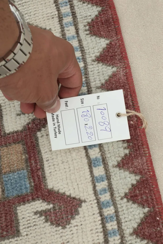 Hand holding a tag showing the dimensions 180x220 cm, confirming hand-made origin.