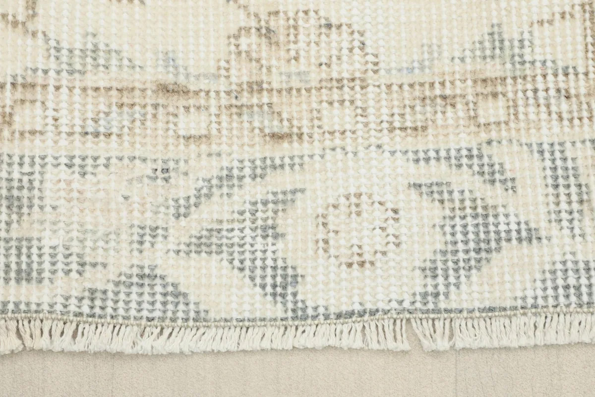 Detail of the rug's fringe and the end border, showing the subtle wear and muted colors.