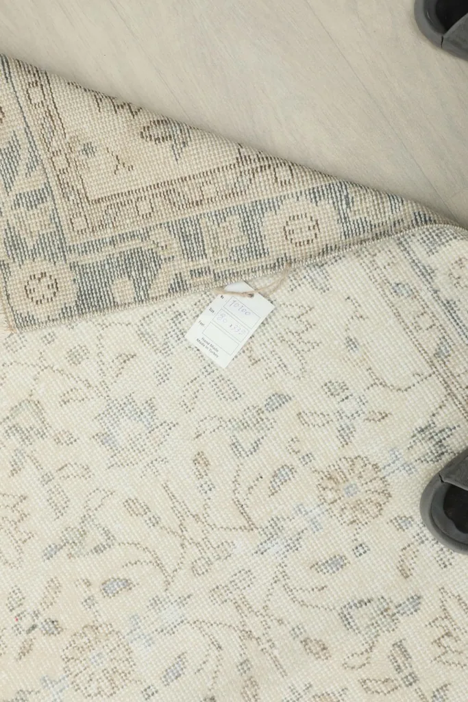View of the rug's back and a small part of the front, with a label visible on the cotton foundation.