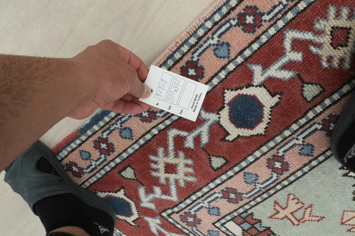 Hand holding a product tag over the rug, showing a close-up of the weave and colors