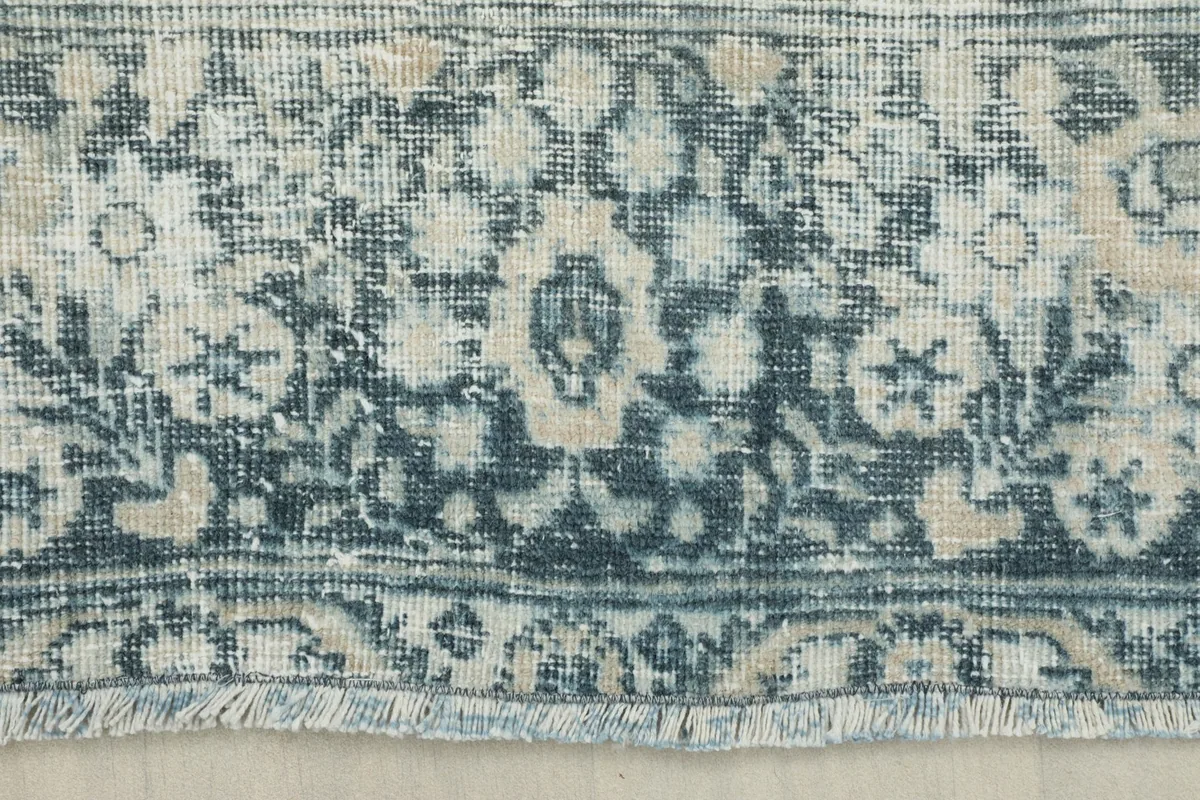Close-up of the rug's border and fringe, showing the hand-knotted texture and a floral motif