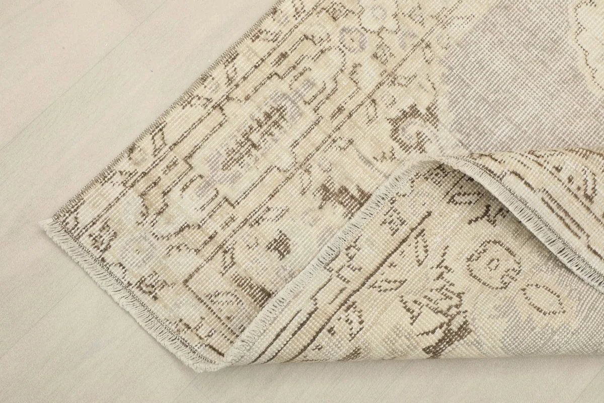 Corner of the rug folded back, showing the cotton foundation and the reverse side of the weave